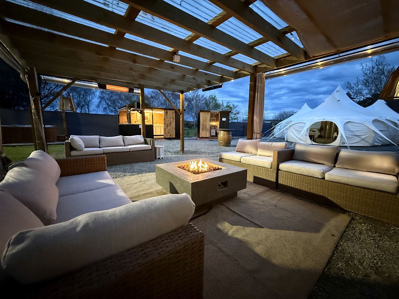 An outdoor patio with wicker furniture, a fire pit, and a covered area with a view of tents.