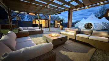 An outdoor patio with wicker furniture, a fire pit, and a covered area with a view of tents.