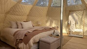 A cozy, triangular tent-style bedroom with a bed, pillows, a bedside table, and a robe rack.