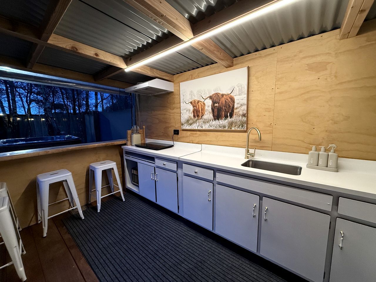 A modern kitchen with a sink, stools, and a painting of yaks.