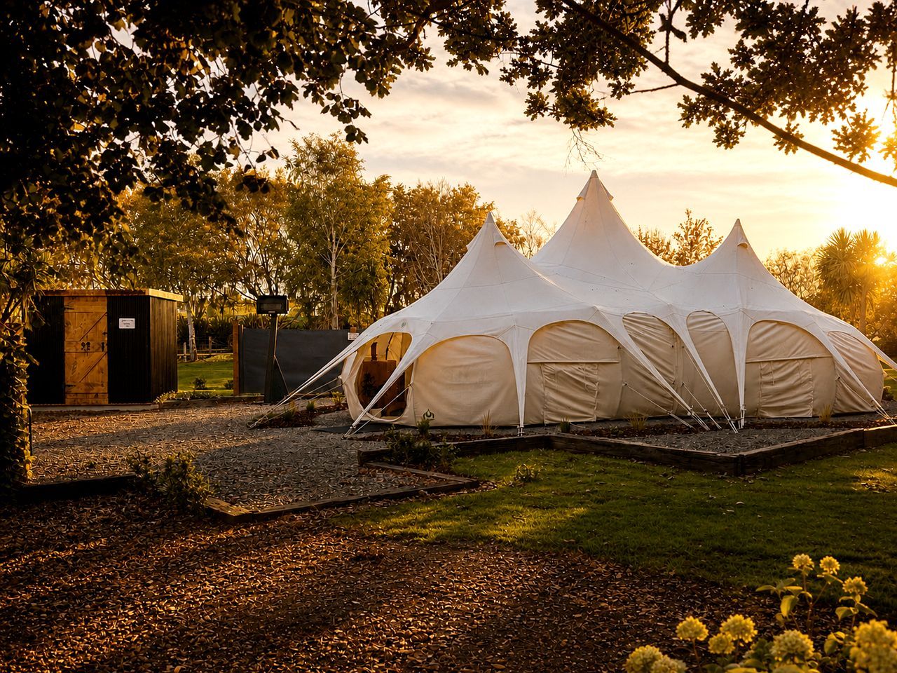 A campsite with three white tents, a wooden structure, and a grassy area with trees.