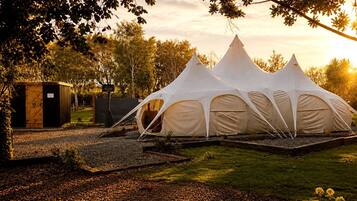 A campsite with three white tents, a wooden structure, and a grassy area with trees.