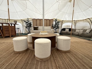 A tented room with a round table, four ottomans, a sofa, and a bookshelf.