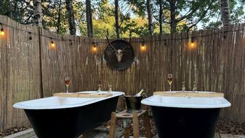Two black bathtubs on a wooden deck with a wooden fence and a deer skull decoration in the background.