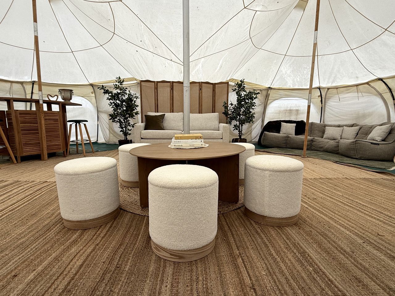 A tented room with a round table, four ottomans, a sofa, and a bookshelf.