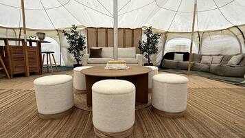 A tented room with a round table, four ottomans, a sofa, and a bookshelf.