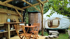 Una terraza de madera con una mesa y sillas, un mueble de madera rústico, y una tienda de campaña al fondo.