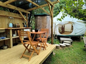 A wooden deck with a table and chairs, a rustic wooden cabinet, and a tent in the background.