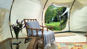 A tent with a wooden chair, a small table, and a vase with flowers.