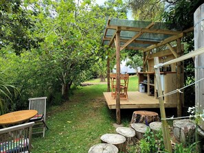 A wooden deck with a table and chairs, surrounded by greenery and trees.