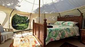 Ein Zelten-Raum mit einem Bett, einem Sessel und Blick auf Grünfläche.