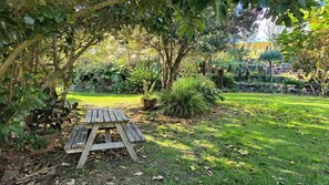 Une table de pique-nique en bois, située dans un jardin où l’on peut admirer différentes plantes et arbres.