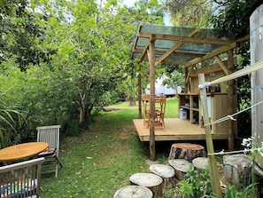 Eine Holzterrasse mit Tisch und Stühlen, umgeben von Grünpflanzen und Bäumen.