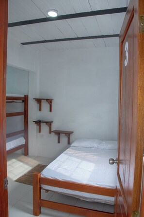 A single wooden bed with a metal door handle, a bunk bed to the left, and a small shelf unit against the wall.
