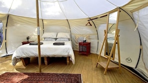 A tent with a bed, a hanging chair, and a small table with a vase.