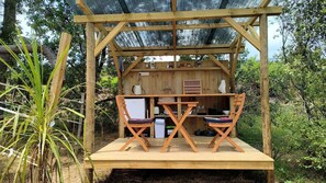 A wooden structure with a table and chairs, a refrigerator, and various kitchen items.