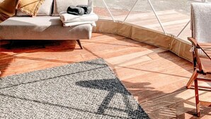 Una tienda con un diseño de ventana geométrico, un sofá con cojines, una silla de madera y una alfombra estampada.