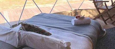 A bed with a view of a mountainous landscape through a geodesic dome structure.