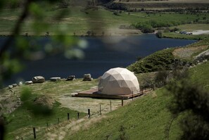 Une structure en forme de dôme, située sur une colline verdoyante, avec un lac en arrière-plan.