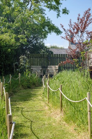 A pathway leading to a wooden bench area with a fence and greenery.