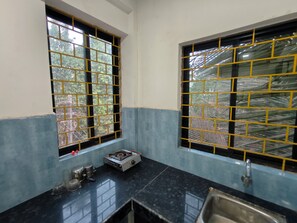 A kitchen with two windows, a gas stove, and a sink. - The Long Stay Goa (Arambol)