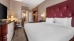 Ein Hotelzimmer mit einem großen Bett, einem Fernseher, einem Schreibtisch mit Stuhl und einem Spiegel.