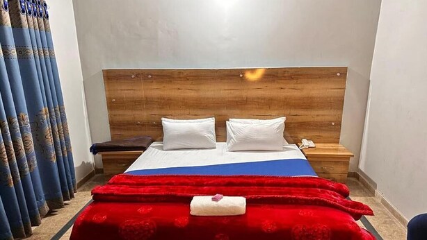 A hotel room with a wooden headboard, a bed with white pillows, a red blanket, and a blue bedspread. - Hotel Shelton One (Multan)