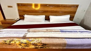 A bed with a wooden headboard, white pillows, and a patterned bedspread. - Hotel Shelton One (Multan)