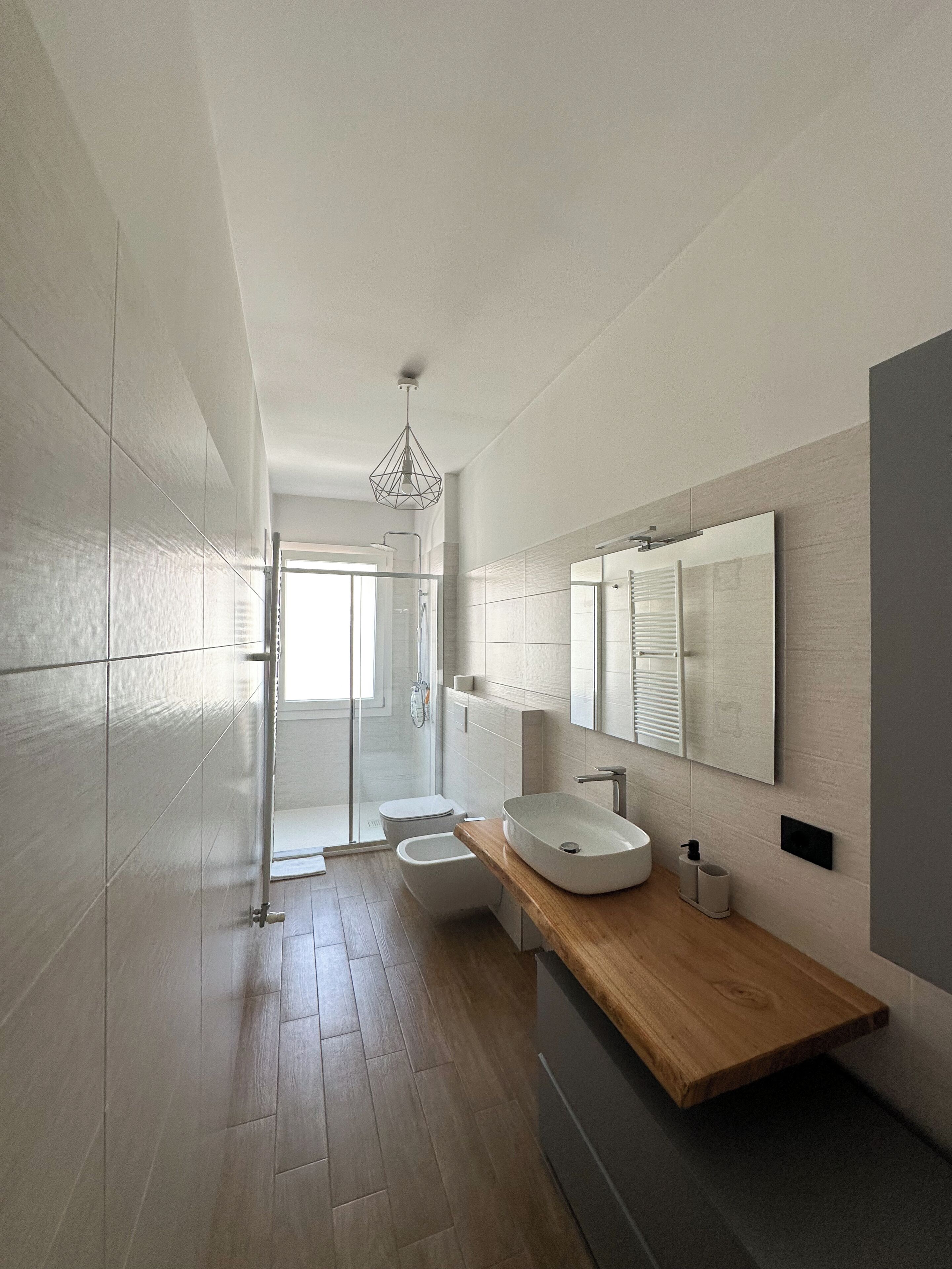 A modern bathroom with a wooden vanity, a large mirror, and a walk-in shower.