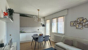 A modern living room with a sofa, a dining table with chairs, a kitchen area, and a large window. - Residenza De Gasperi - Location within walking distance of Treviso and Venice (Preganziol)