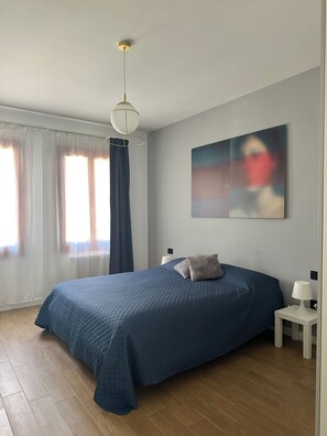 Un dormitorio con una cama grande, una mesita de noche, una lámpara colgante y un cuadro en la pared.