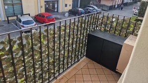 A balcony with a view of parked cars and buildings, including a pharmacy and a residential building. - Residenza De Gasperi - Location within walking distance of Treviso and Venice (Preganziol)