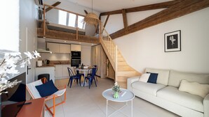 Un appartement moderne de style « loft », comprenant une cuisine, un coin repas et un salon, et caractérisé par des poutres apparentes et un escalier.