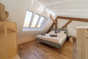 A bedroom with a sloped ceiling, wooden floor, a bed with pillows, a nightstand, and a window.