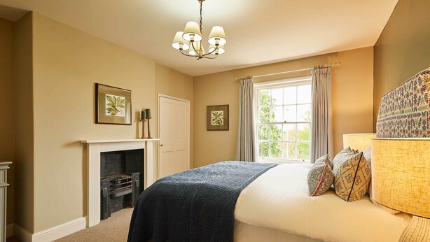 Un dormitorio con cama, chimenea, ventana con cortinas y candelabro.