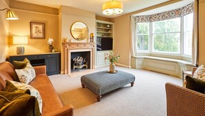 Una sala de estar con sofá, reposapiés, chimenea y ventana grande.