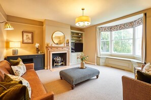 A living room with a sofa, ottoman, fireplace, and large window. - Host & Stay - Tree Tops (Middleton One Row)