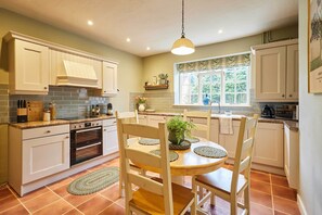 A kitchen with white cabinets, a wooden dining table, and a hanging light fixture. - Host & Stay - Tree Tops (Middleton One Row)