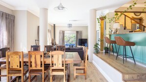 Un vaste espace dédié à la salle à manger, avec des chaises en bois et une grande table, un bar avec des tabourets, et une vue sur l’extérieur.