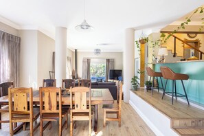 A spacious dining area with wooden chairs and a large table, a bar with stools, and a view of the outdoors. - Greenview Villa -holiday home (Cape Town)