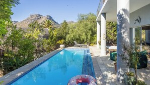 Une piscine avec vue sur les montagnes, entourée de verdure et dotée d’une terrasse avec des chaises longues.