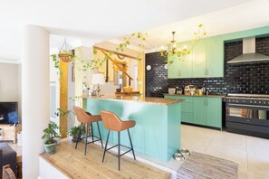 A modern kitchen with a central island, bar stools, and a dining area with a wooden floor. - Greenview Villa -holiday home (Cape Town)