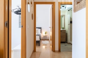 A hallway leading to a bedroom with a bed, bedside table, and a small plant.