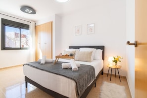 A hotel room with a bed, a bedside table with a lamp, a window, and a door.