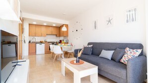 Ein modernes Wohnzimmer mit einem grauen Sofa, einem weißen Couchtisch und einem Essbereich mit weißem Tisch und Stühlen.