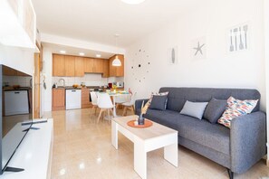 A modern living room with a grey sofa, white coffee table, and a dining area with a white table and chairs.