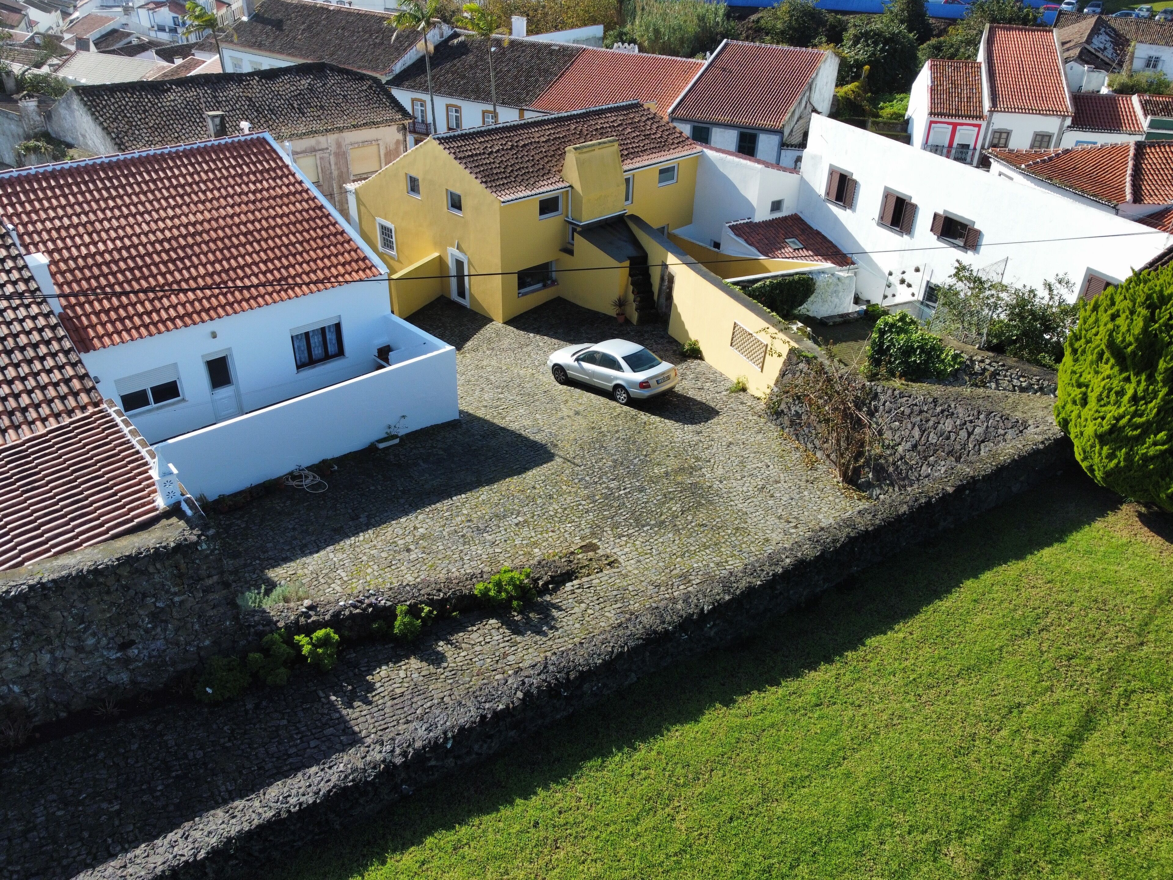 En vy över ett bostadsområde från ovan, med hus som har röda tegeltak och en blandning av vita och gula fasader. En vit bil står parkerad på uppfarten till ett gult hus.