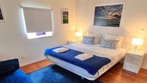 Un dormitorio con cama, mesitas de noche, un sofá azul y un cuadro en la pared.