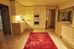 Une cuisine avec des meubles blancs, un tapis rouge et un pare-feu en pierre.