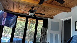 Una habitación con techo de madera, ventiladores de techo, televisión y vista al exterior.
